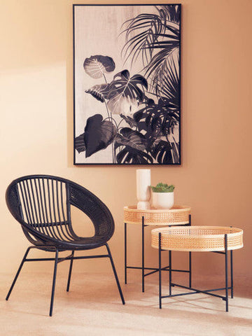 Black woven rattan chair with slender metal legs shown next to the fia white planter for stylish indoor decor