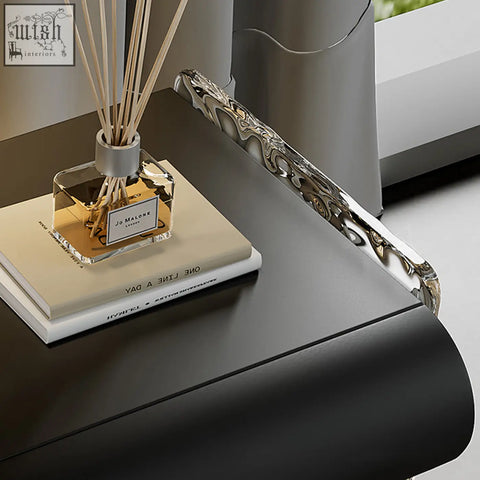 A sleek silver-toned metal figueroa bedside table with storage and a flowing abstract wave design edge