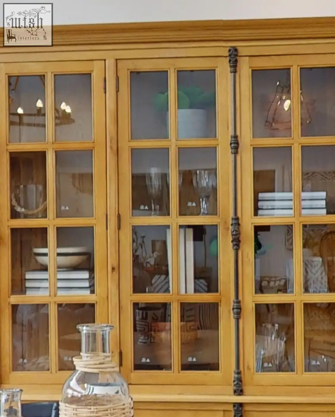 A warm-toned wooden display cabinet with glass doors and ornate black handles showcasing fiori small succulent with natural stone base