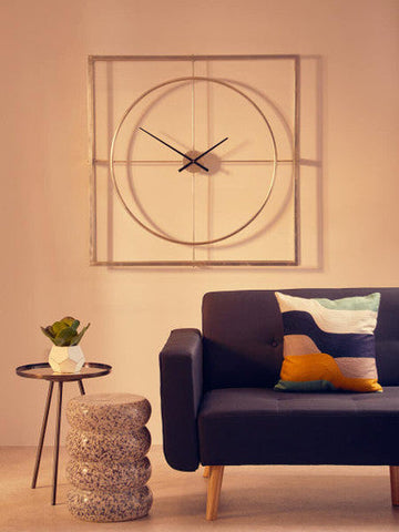 A modern geometric wall clock with a metallic frame and thin black hands next to a fiori white cement pot succulent