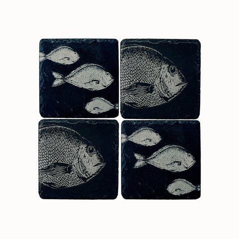 Set of four dark slate coasters with light gray engraved fish designs perfect for stylish drink protection