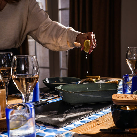 A hand squeezing a yellow lemon with juice dripping over a slate table runner on a slate table