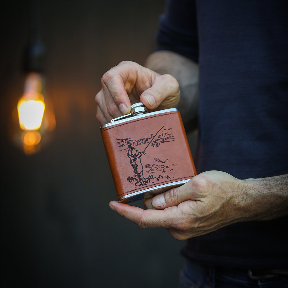 Brown leather hip flask with silver cap featuring engraved fisherman illustration perfect for fishing trips