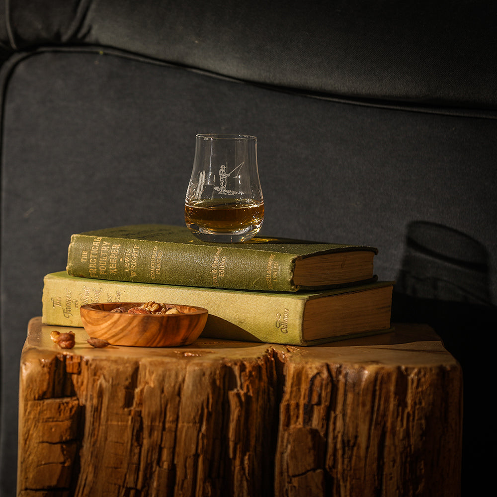 A clear glass perfect measure tasting glass with amber whisky and subtle etched fishing figure design