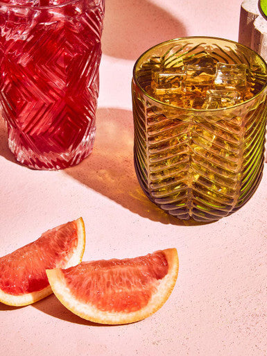 Amber-colored glass tumbler with ribbed texture and ice cubes from the fleur set of four green tumblers collection