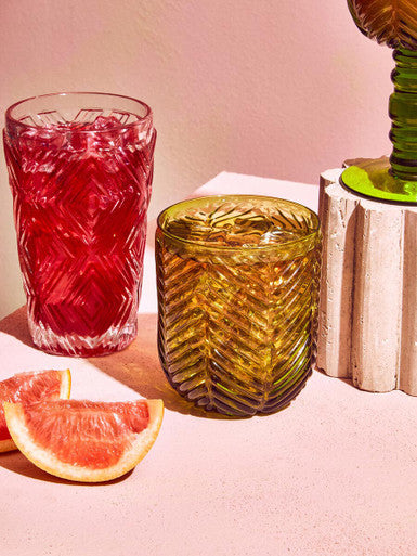Clear glass tumblers from the fleur set with intricate etching one filled with red liquid the other amber-colored