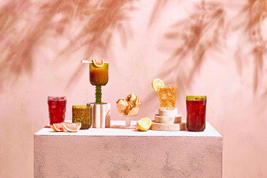 A fleur set of four green tumblers with colorful modern cocktail glasses featuring unique designs and vibrant liquids