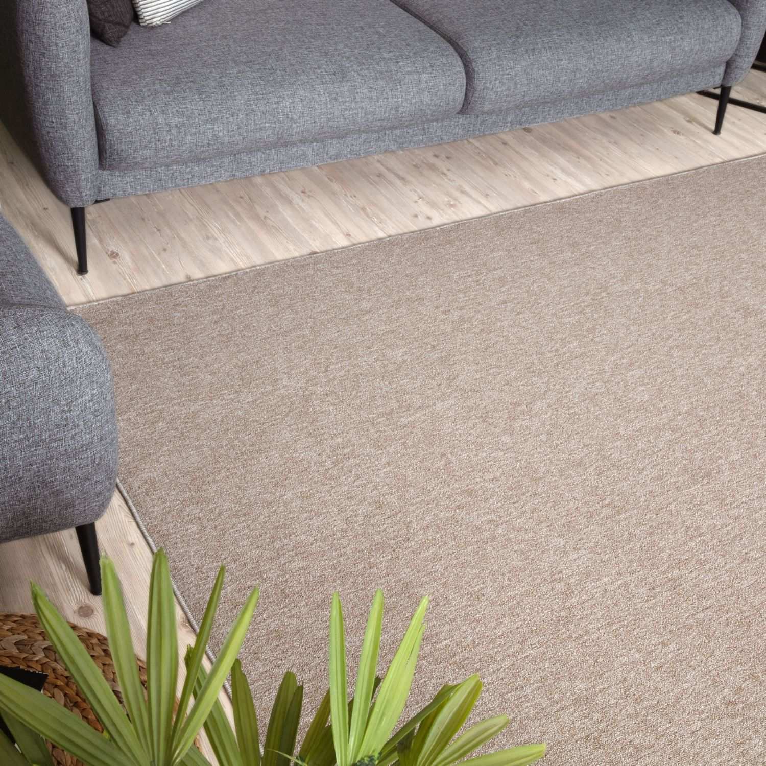 Beige low pile flex beige low rug with subtle woven texture under a gray sofa on light wood flooring