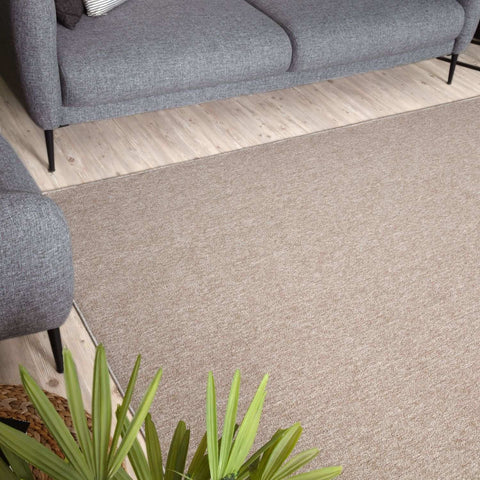 Beige low pile flex beige low rug with subtle woven texture under a gray sofa on light wood flooring