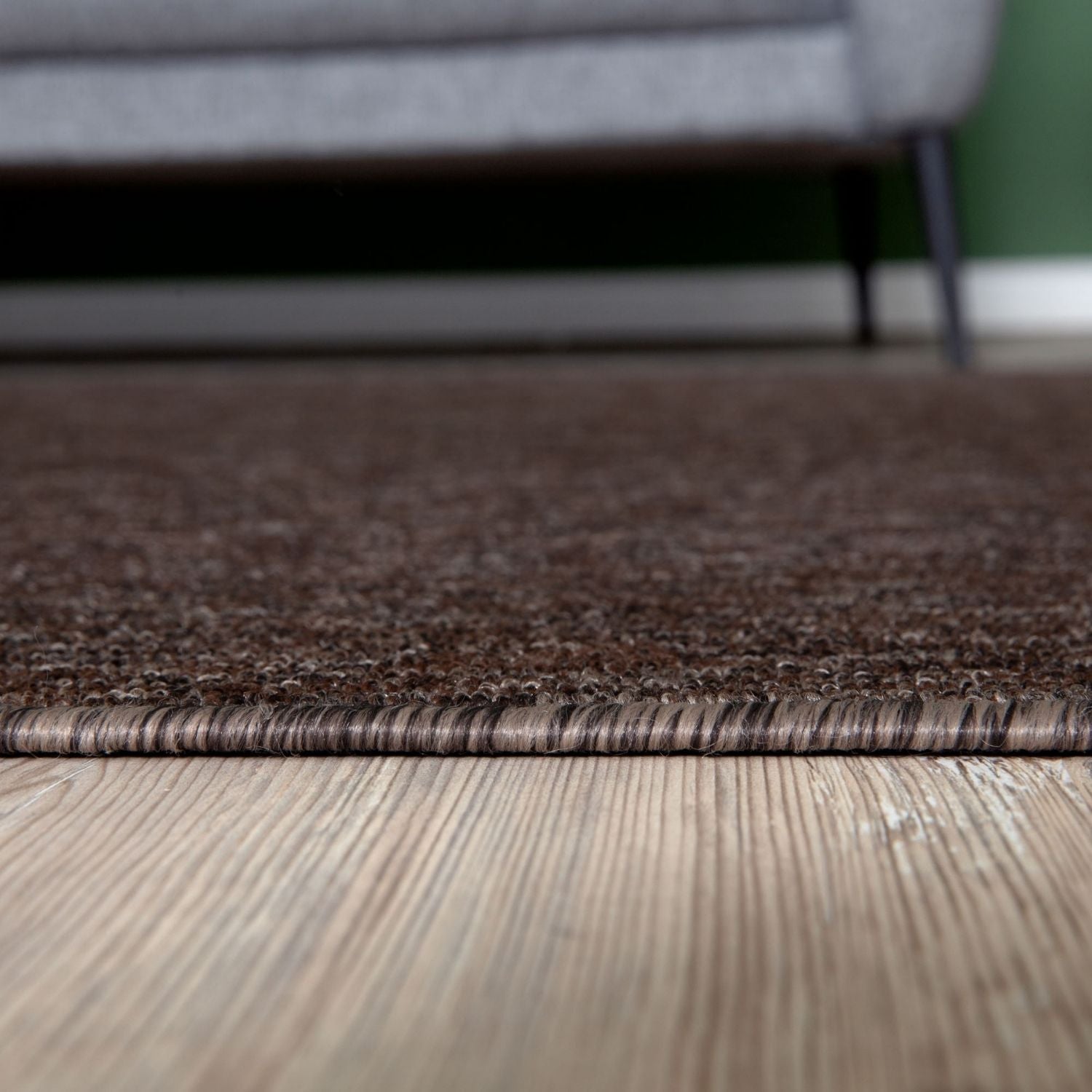 Brown low pile textured rug with woven edge on light wood floor perfect for cozy living spaces