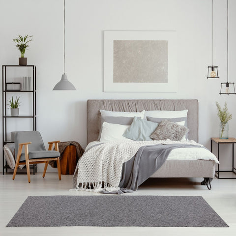 Gray upholstered bed with tufted headboard and layered bedding on a flex grey low pile solid rug