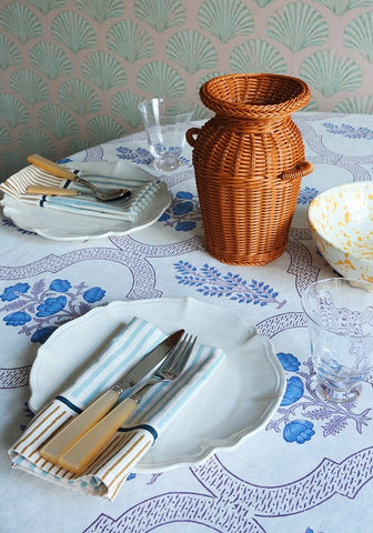 A woven orange wicker vase with two handles paired with a blue flora tablecloth for a cozy decor look