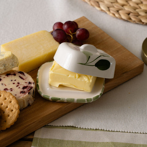 White ceramic mini ceramic butter dish with green leaf and olive design and matching lid covering yellow butter