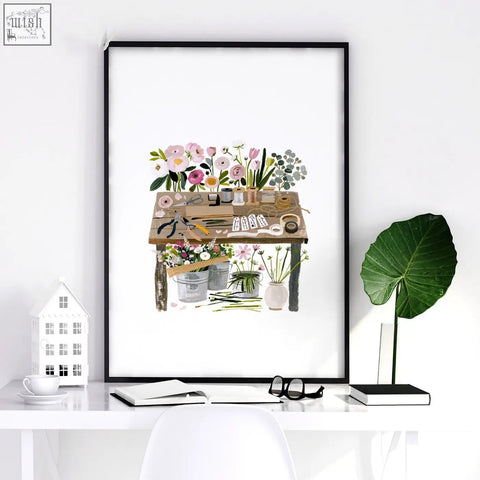 A framed floral art illustrated print set of 3 featuring a rustic wooden table with gardening tools in pastel tones for country cottage decor