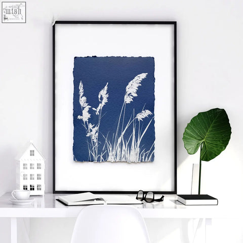 A framed cyanotype floral art wall print with white grass silhouettes on indigo background in a sleek black frame