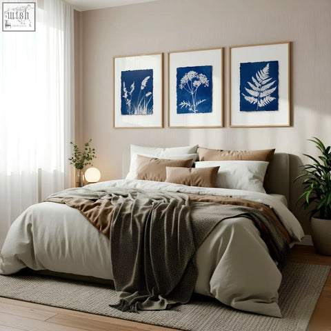 A cozy bed with beige and brown linens and dark gray throw below a floral art wall set of 3 cyanotype prints