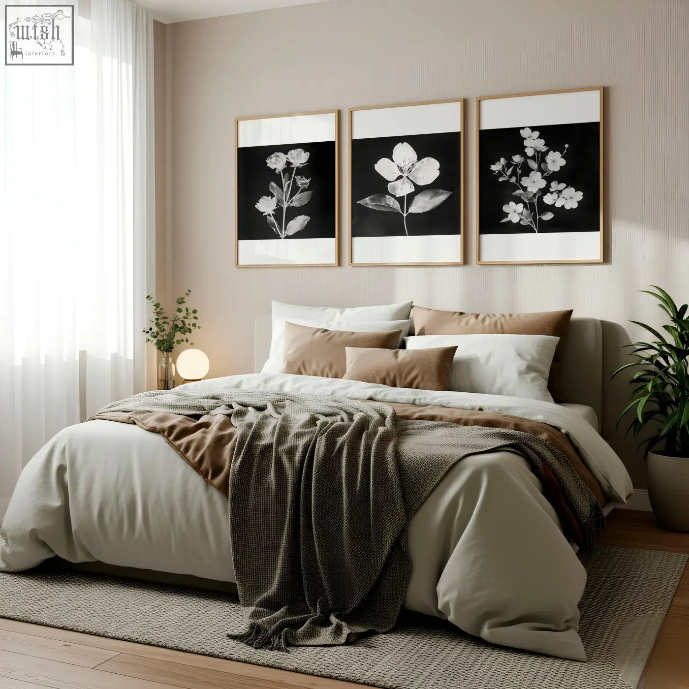 A cozy bed with soft beige and brown linens and a dark gray throw next to charcoal and white floral wall art prints