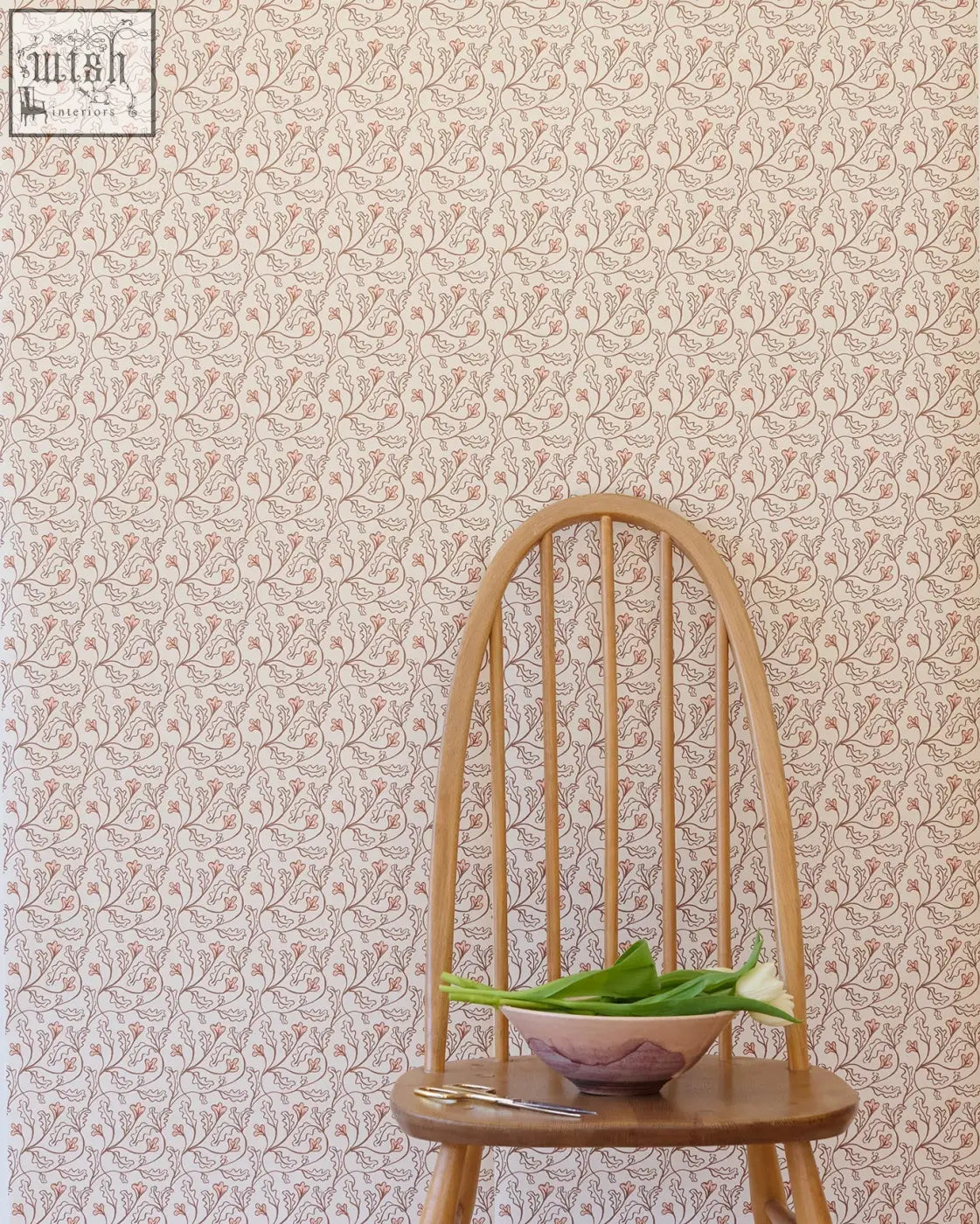 A light wood chair with curved back and vertical spindles holding a bowl of green leaves against florence wallpaper shell small repeat