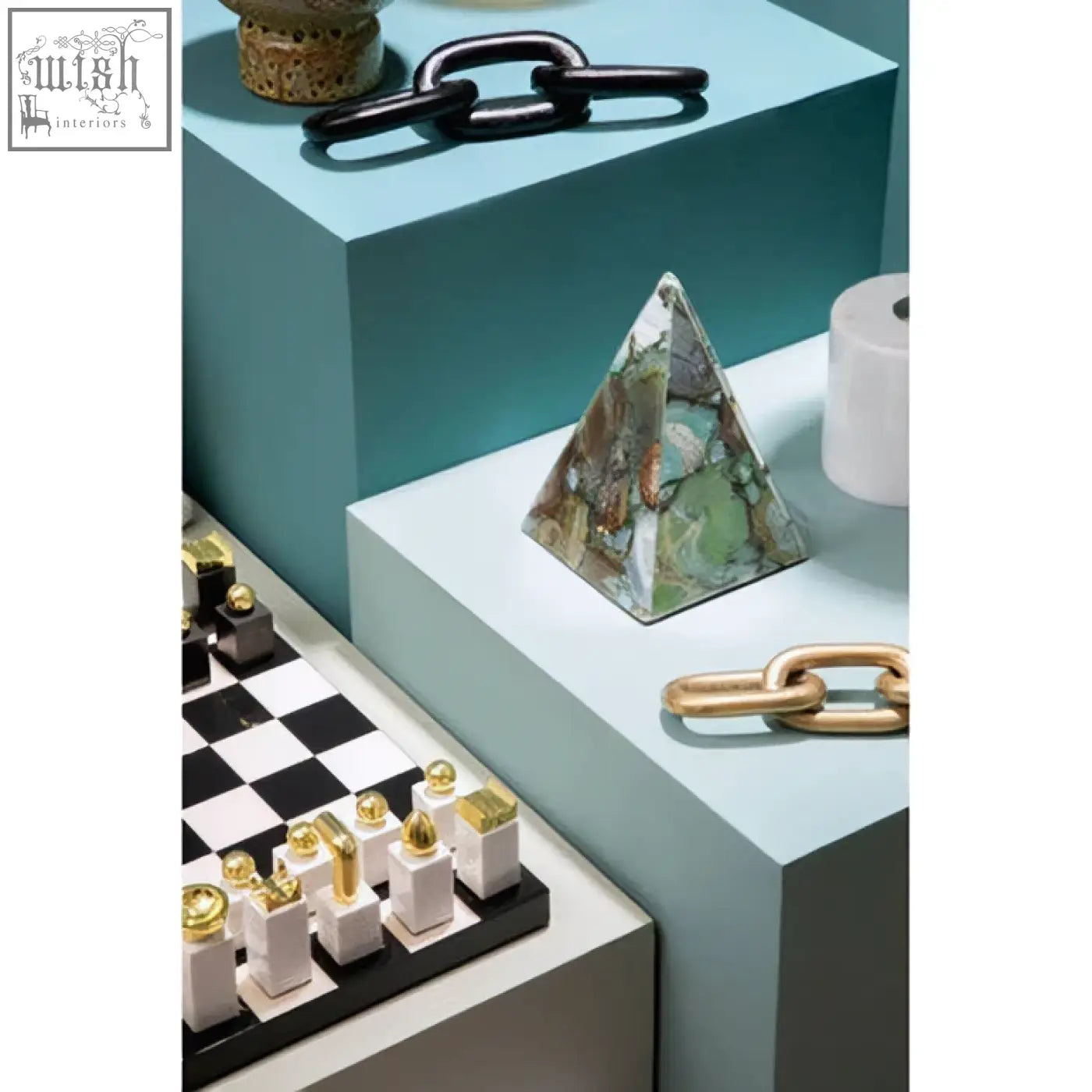 A flos marble and wood chess set piece shaped like a green and brown marbled triangular pyramid on a light blue pedestal