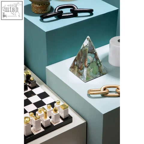 A flos marble and wood chess set piece shaped like a green and brown marbled triangular pyramid on a light blue pedestal