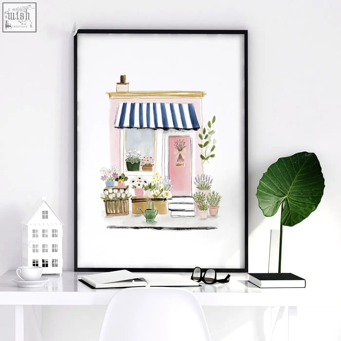 A framed watercolor flower art wall print of a charming pink flower shop with blue and white striped awning in black frame