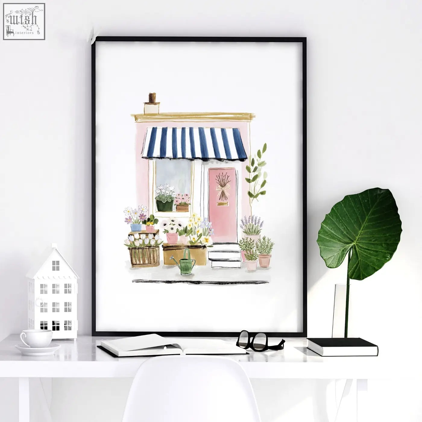 A framed watercolor flower art print of a pink flower shop with blue and white striped awning for wall decor