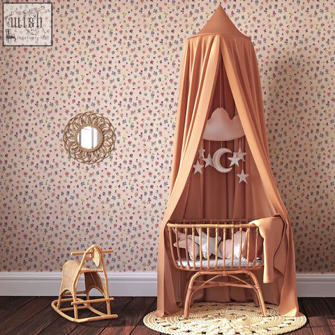 A soft peach canopy bed with woven rattan frame and hanging celestial decor featuring flower power rainbow wallpaper