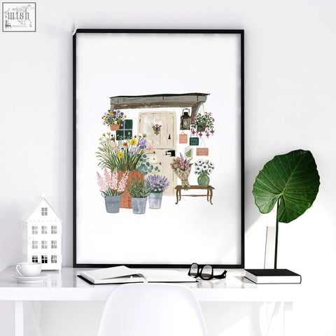 Black-framed flower print wall art showing a charming flower shop scene with vibrant blooms in pots and baskets
