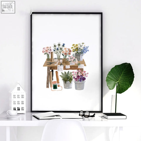 Black-framed flower print wall art showing rustic wooden table with potted flowers and gardening tools for flower shop decor