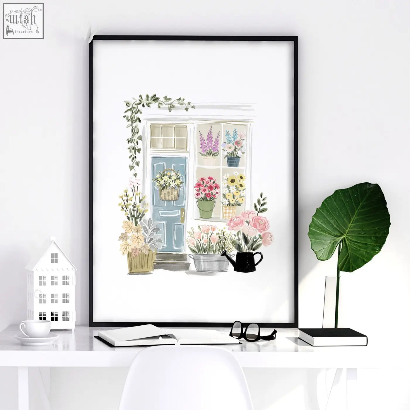 A framed watercolor flower print of a charming country cottage flower shop with a blue door and vibrant blooms in black frame
