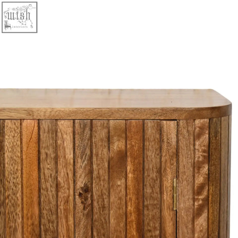 A warm-toned mango wood fluted curve chest of drawers with vertical slats and curved top edge showing grain patterns