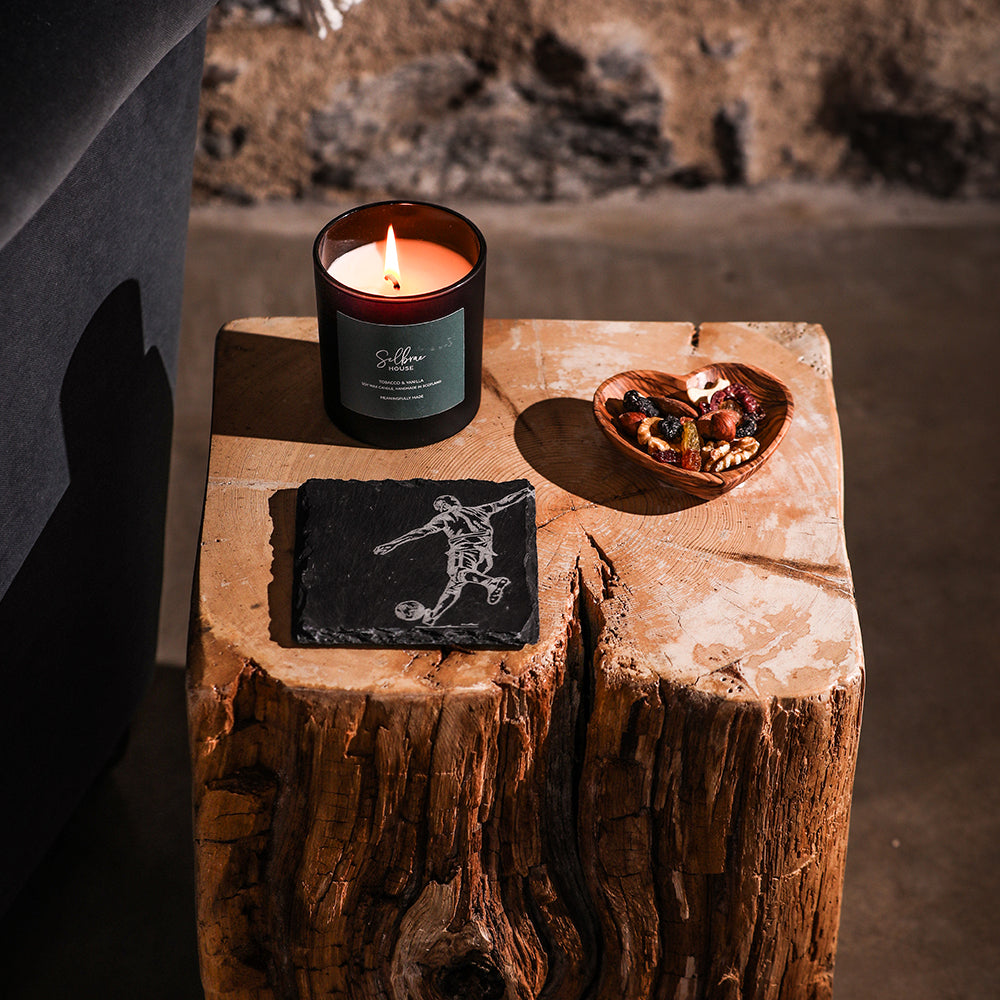 Lit amber glass candle with dark green label and silver wick on a football single slate coaster slate coaster
