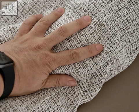 A hand rests on the off-white and dark gray linen fabric of the foster four seater corner sofa showcasing its textured weave