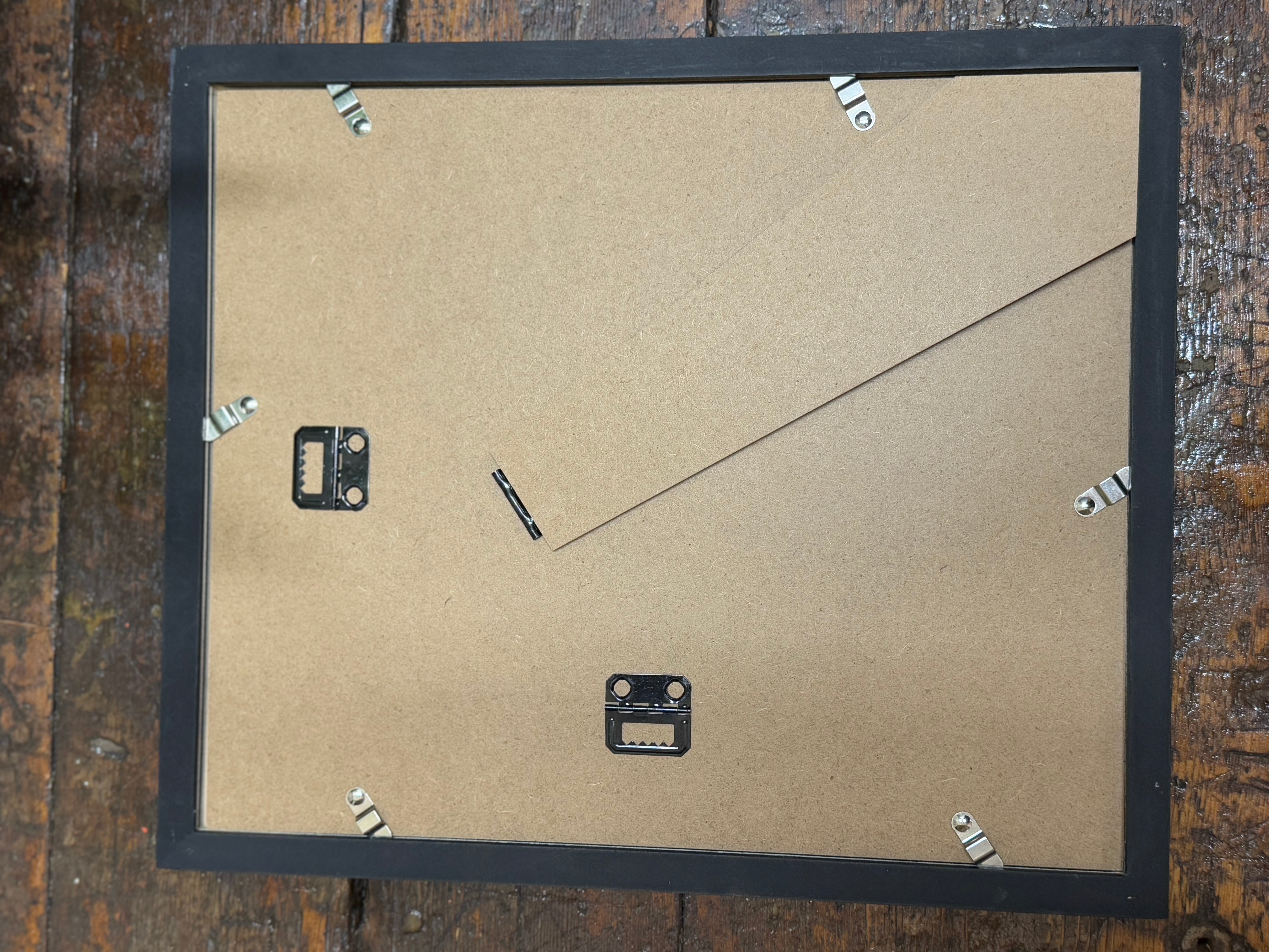 Black rectangular picture frame showing the back with cardboard and metal hanging hardware for 1920s medical book plate art