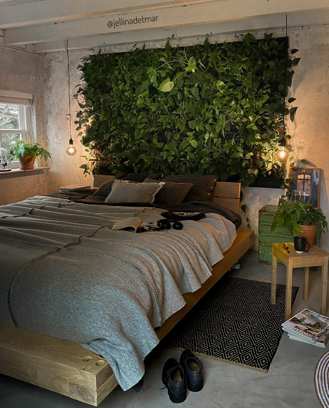 Wooden bed with gray textured bedding and a lush green living wall featuring a frameless plant cassette system