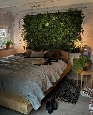 Wooden bed with gray textured bedding and a lush green living wall featuring a frameless plant cassette system
