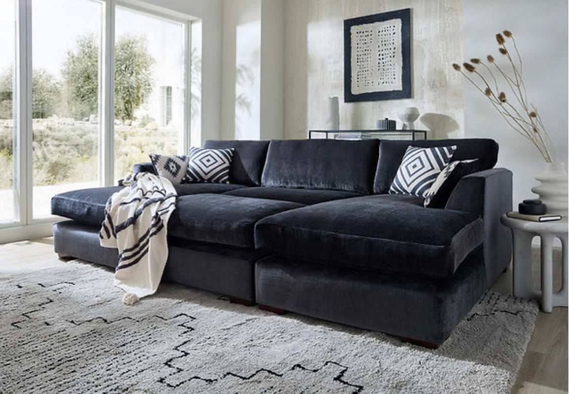 Black velvet freedom sofa double chaise with geometric pillows and matching stool in a cozy living room setup