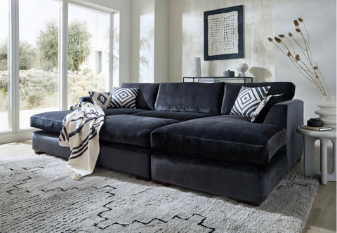 Black velvet freedom sofa double chaise with geometric pillows and matching stool in a cozy living room setup