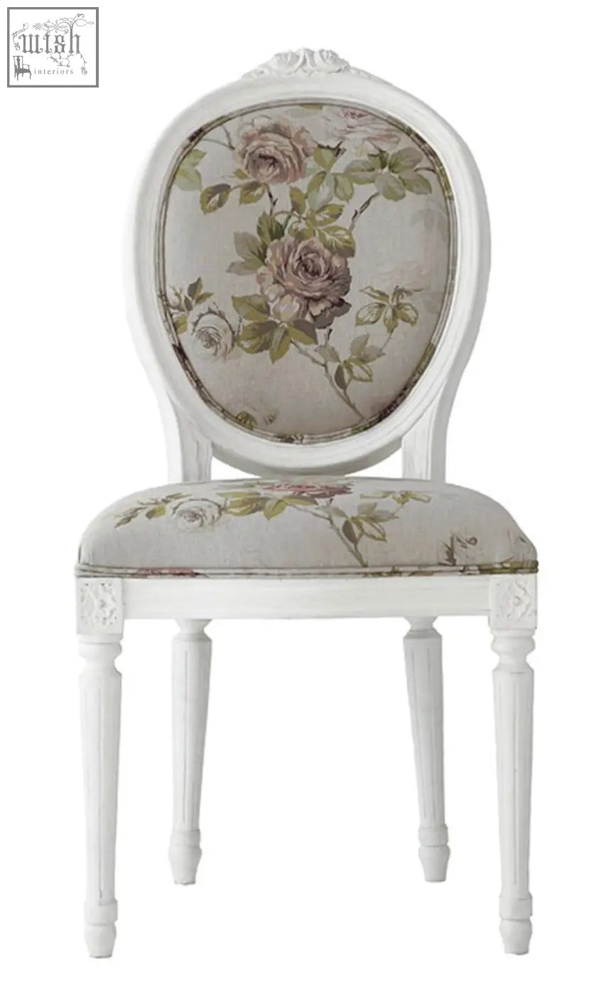 A white upholstered french oval back chair with a floral pattern in muted rose and green tones