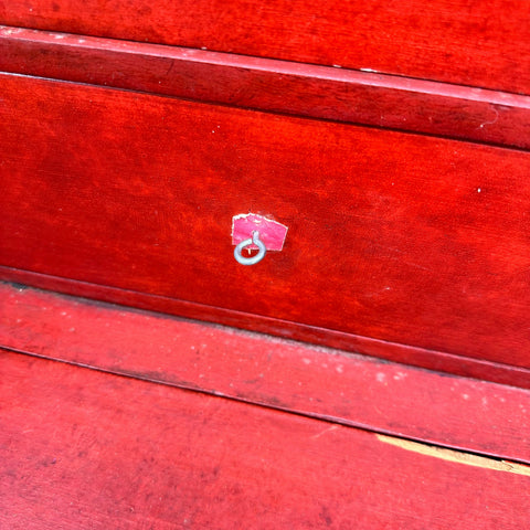 Small silver metal ring on torn pink sticker on red wood secretaire d’abattant vintage cupboard detail