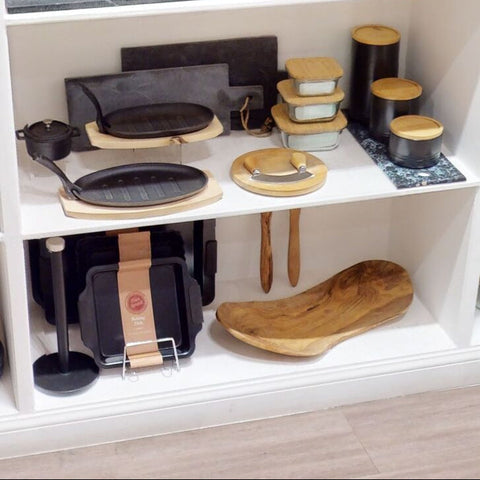 A sleek black cast iron griddle with wooden handle and base beside a freska 520ml glass container with bamboo lid