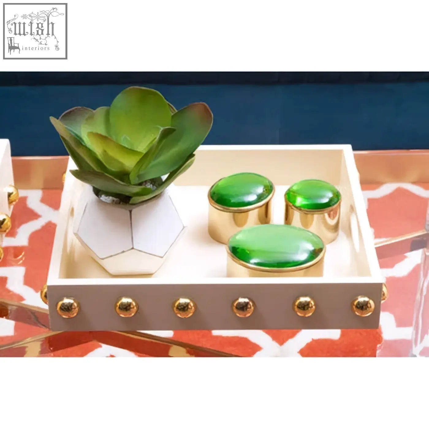 A cream serving tray with gold studded edges holding a white geometric planter and three green oval containers