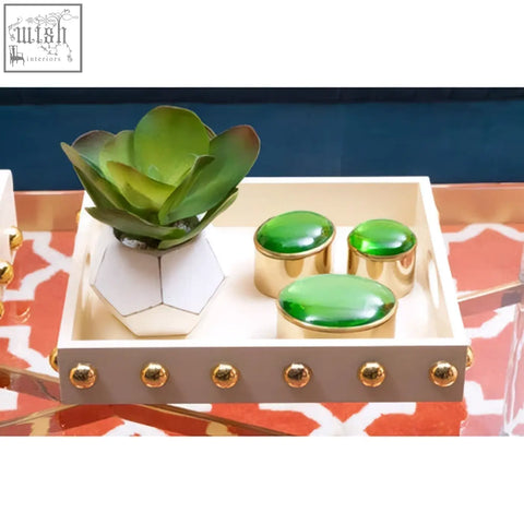 A cream serving tray with gold studded edges holding a white geometric planter and three green oval containers
