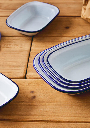 Stack of white enamel rectangular pie dish plates with bold blue rims neatly arranged on wooden surface