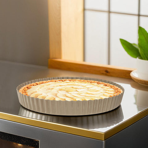 A golden-brown apple tart baked in a silver-colored scratch flan tin with a removable base and fluted edges