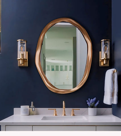 Gold-toned fronchi mirror with irregular shape and sleek metallic frame mounted above a white vanity