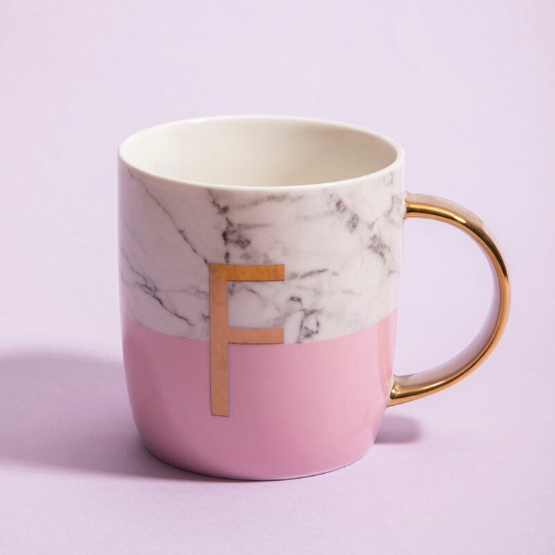 A pink and white marble effect ceramic monogram mug with a gold frosted deco handle and letter f on the side