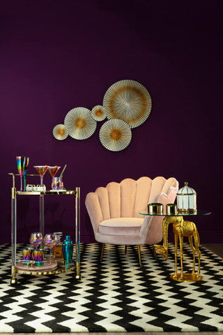 A plush blush pink scalloped velvet armchair with gold tone legs shown next to frosted deco set of 4 tumbler glasses