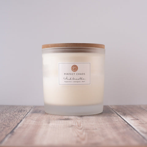 A creamy white frosted glass candle with a natural wood lid featuring peppermint lemongrass basil essential oils and long burn time