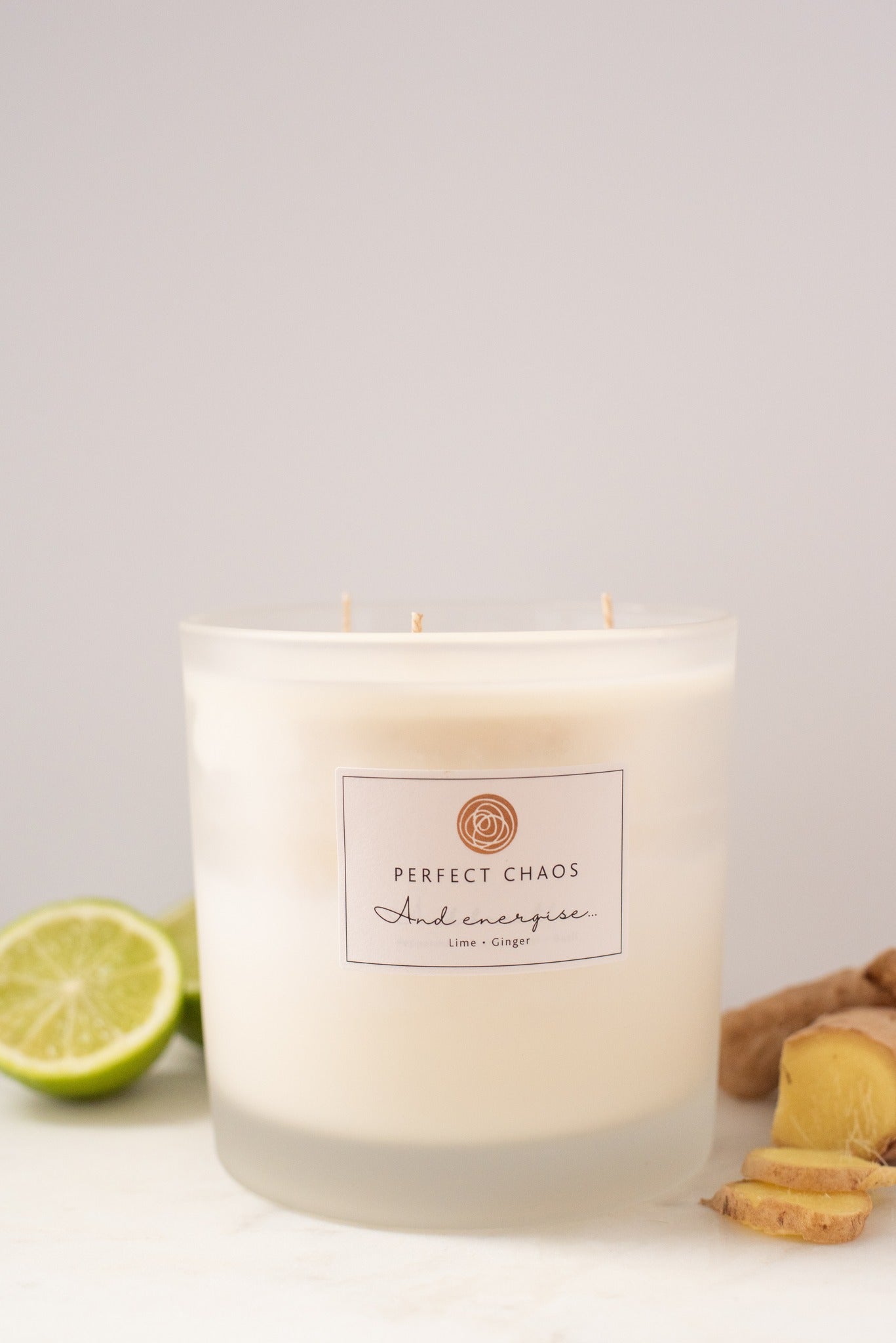 A frosted glass candle jar with three wicks labeled perfect chaos scented with lime and ginger with long hours burn time